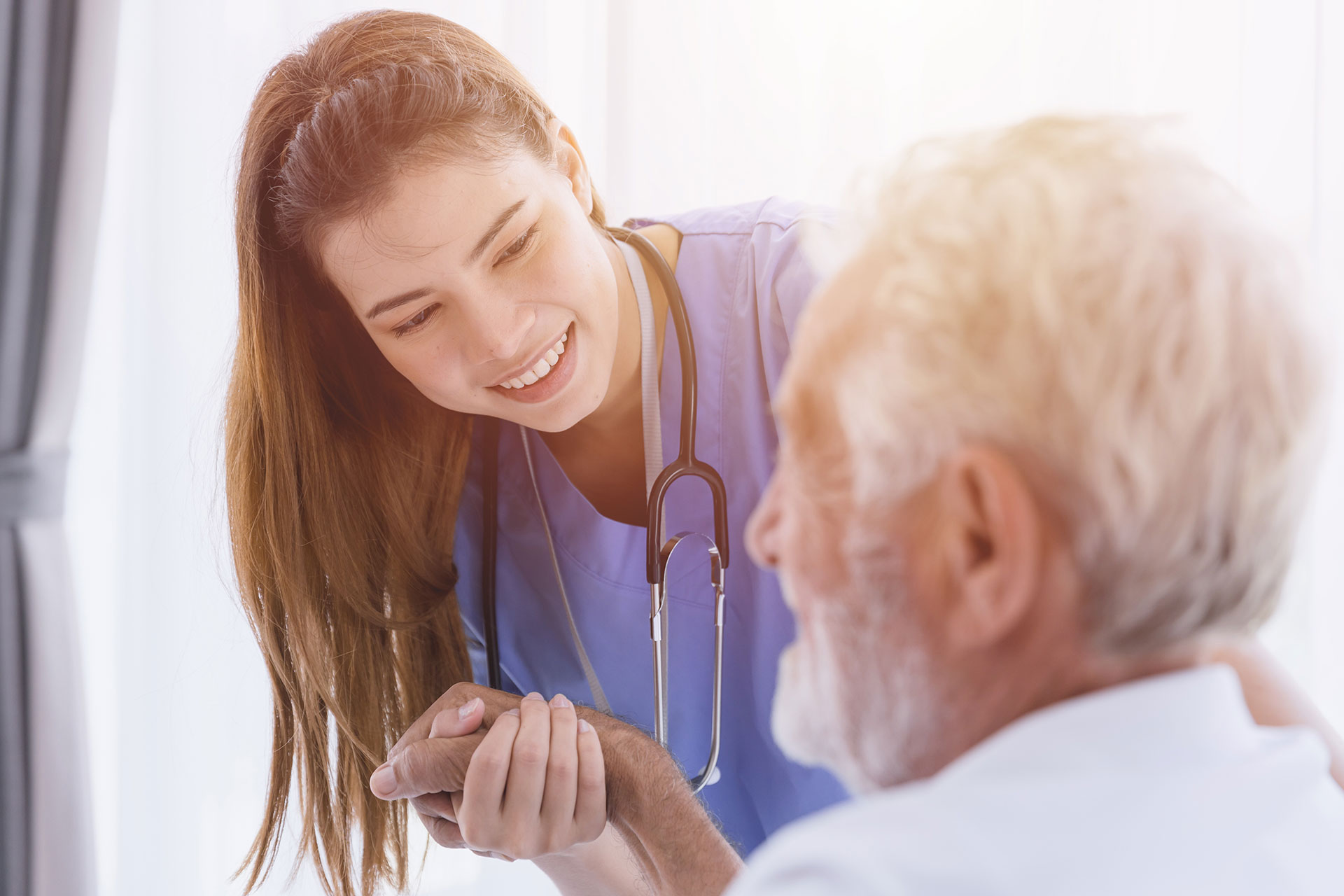 Smiling nurse in blue scrubs engaging with an elderly patient, demonstrating Cliniconex’s commitment to enhancing patient Experience.