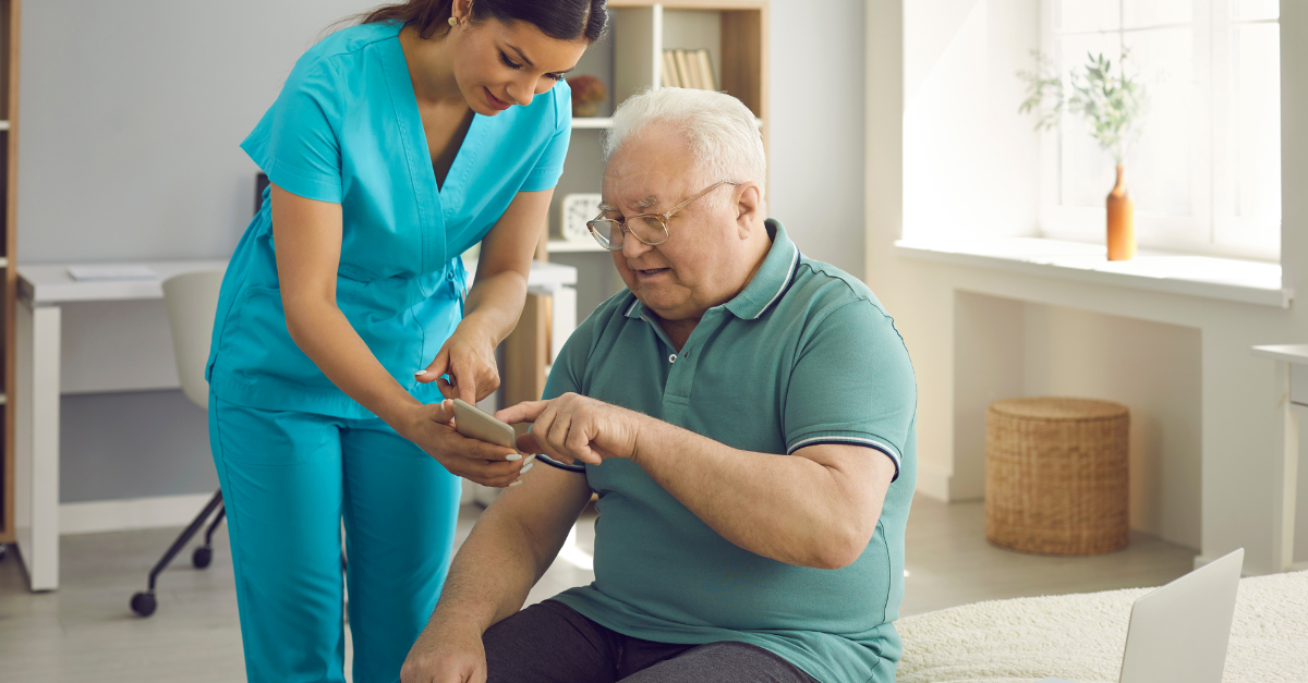 A healthcare worker assists an elderly man using a smartphone, illustrating how technology like AI is improving the resident experience in senior living communities.